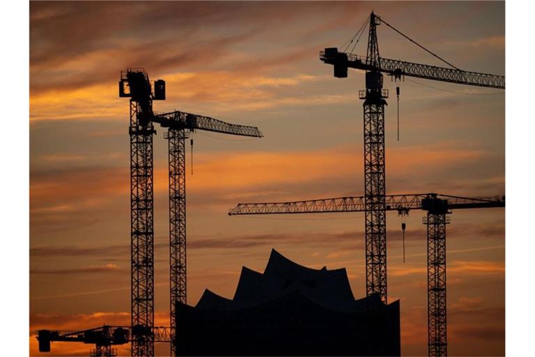 Die Kräne verschiedener Baustellen in der Hamburger Hafencity zeichnen sich im Sonnenuntergang vor der Elbphilharmonie ab. Foto: Christian Charisius/dpa
