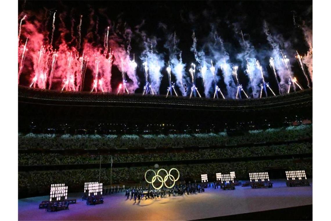 Die Olympischen Ringe leuchten unter buntem Feuerwerk. Foto: Swen Pförtner/dpa