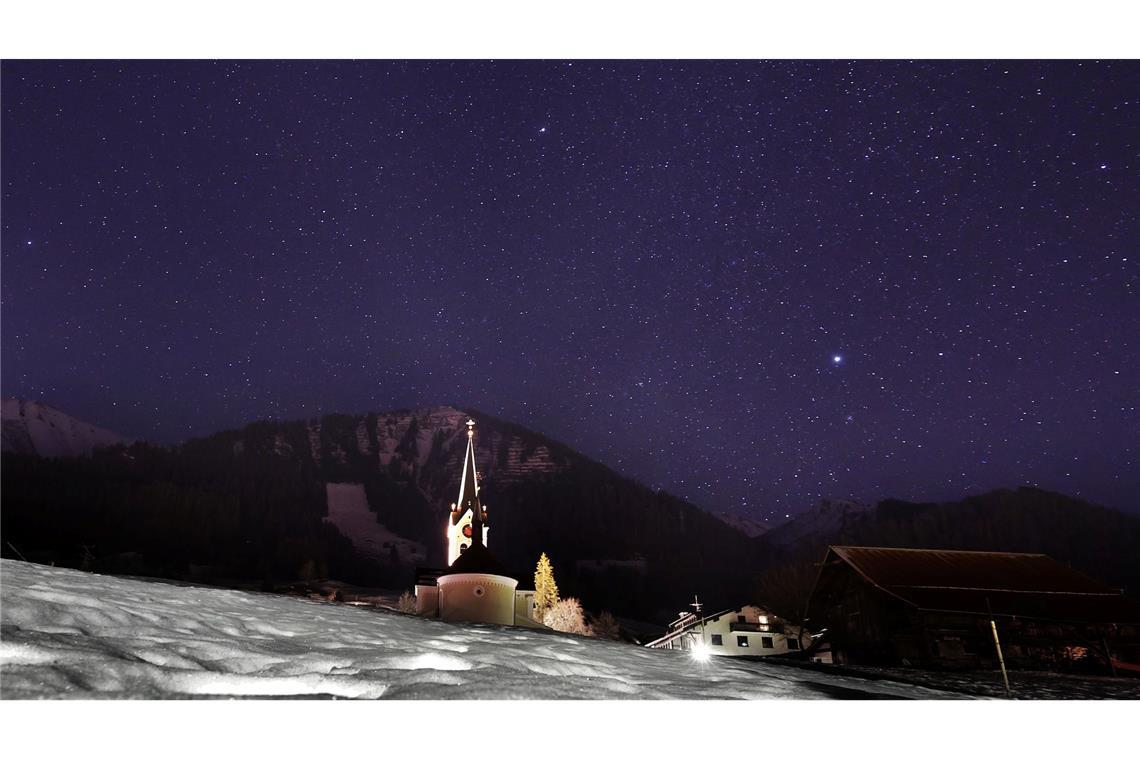 Bilder des Tages Die Pfarrkirche Mariä Opferung steht in Riezlern unter dem Sternenhimmel hinter einer schneebedeckten Wiese.