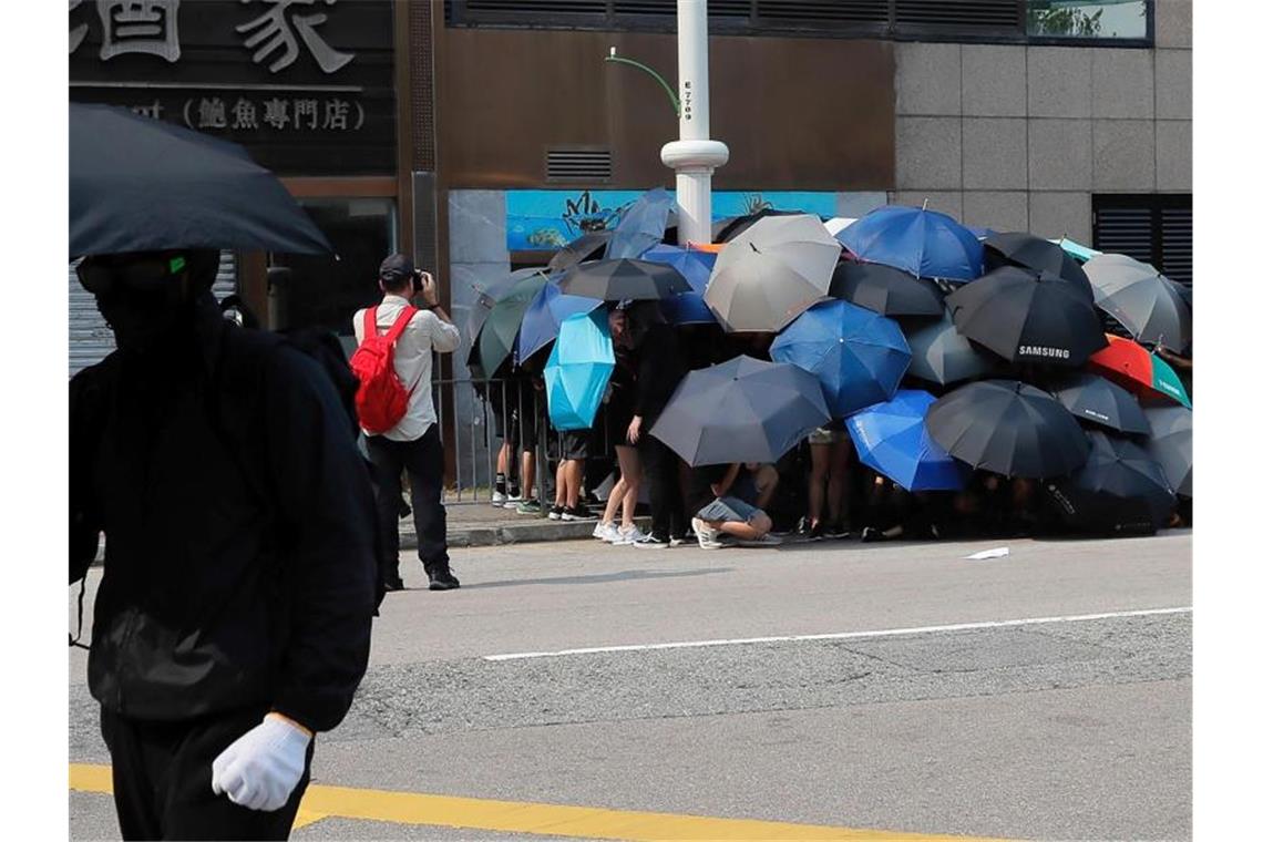 Neue Zusammenstöße in Hongkong - Wasserwerfer auf der Straße Die Schirme von Hongkong: Regierungskritische Demonstranten schützen sich damit nicht nur vor Tränengas, sondern auch vor Überwachungskameras. Hier versuchen sie, eine Kamera zu demontieren. Foto: Kin Cheung/AP