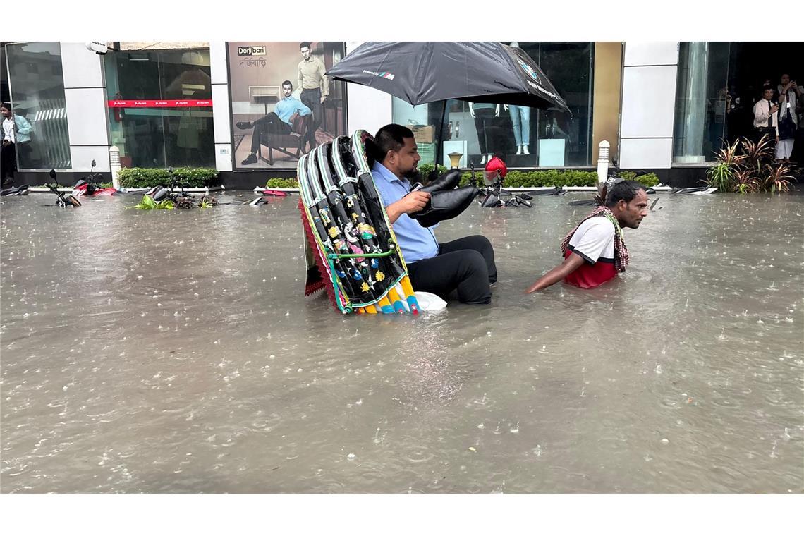 Die Schuhe bleiben trocken: Ein Mann lässt sich in Bangladesch in einer Rikscha durch eine überflutete Straße fahren.