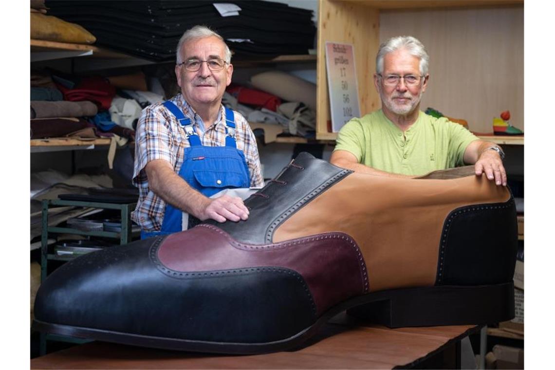 Die Schuhmachermeister Matthäus Jörg (l) und Johannes Schunk stehen hinter einem überdimensionierten Schuh. Foto: Marijan Murat/dpa