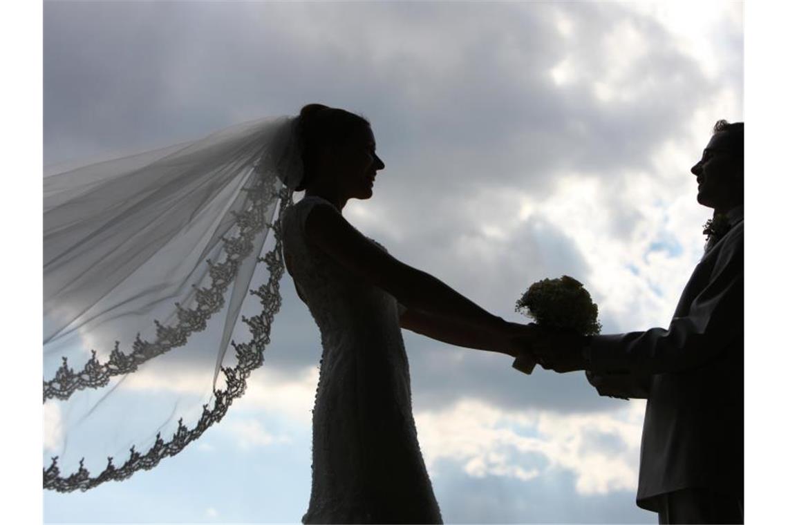 Die Silhouette eines frisch vermählten Hochzeitspaares zeichnet sich im Gegenlicht ab. Foto: Patrick Pleul/Archivbild