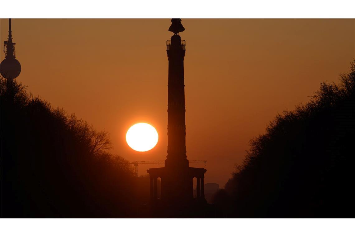 Die Sonne geht am Morgen bei wolkenlosem Himmel hinter der Siegessäule in Berlin auf.