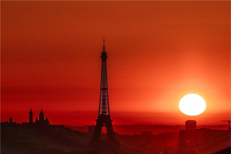 Die Sonne geht Anfang Juli 2025 über dem Eiffelturm und der Basilika Sacre Coeur auf dem Montmartre-Hügel auf, während in der Stadt wegen der hohen Temperaturen Alarmstufe Rot herrscht: