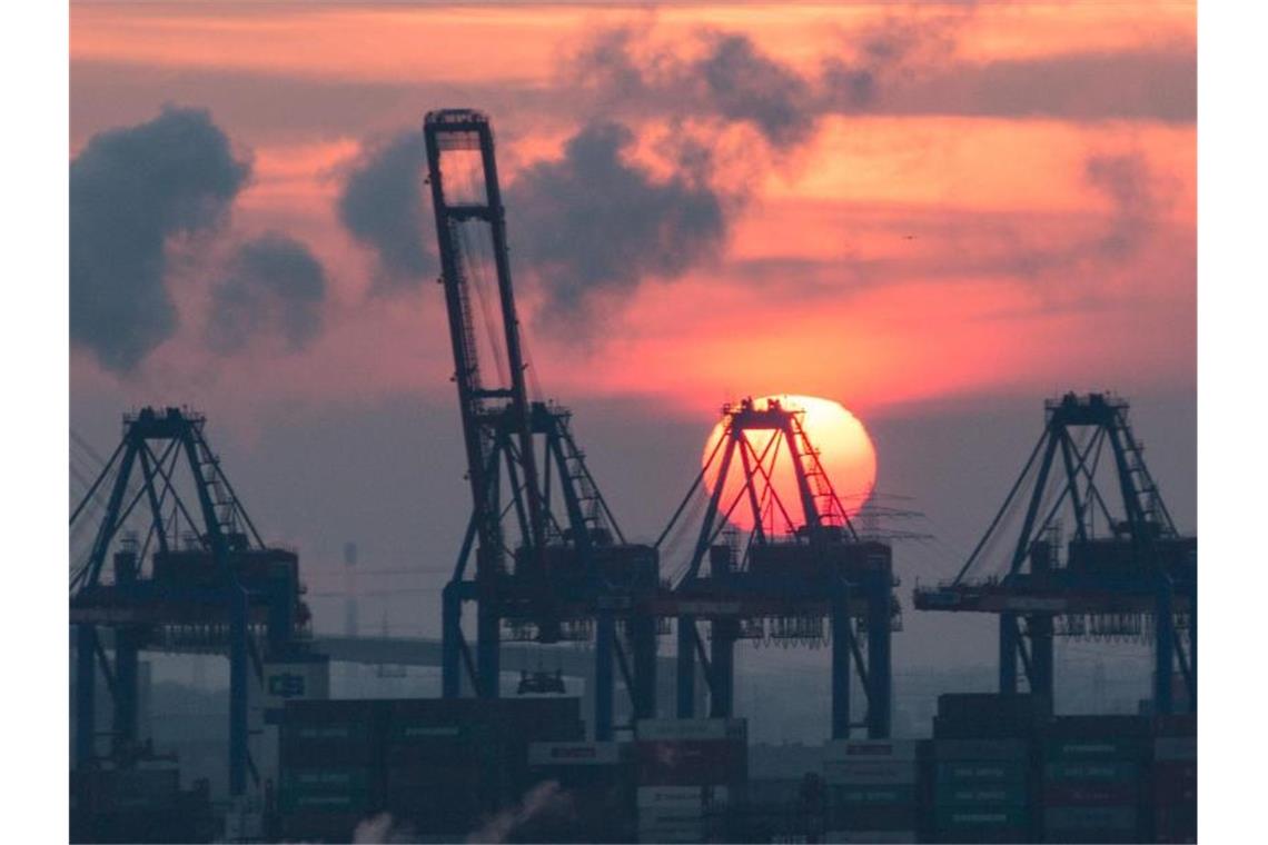 Die Sonne geht im Hafen hinter den Containerbrücken des HHLA Containerterminal Tollerort unter. Foto: picture alliance / Christian Charisius/dpa