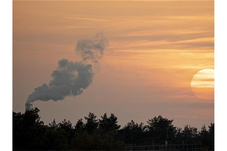 Die Sonne geht neben einem rauchenden Schornstein unter. Die Grenzwerte für den Ausstoß von Schadstoffen aus vielen Industrieanlagen werden strenger. Foto: Fabian Sommer/dpa