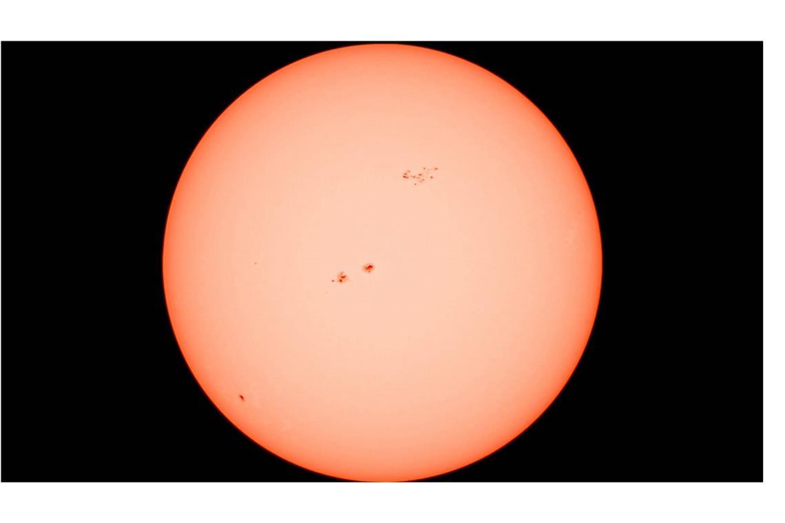 Die Sonne in all ihrer Kraft aufgenommen durch ein Teleskop mit Sonnenfilter. Deutlich sichtbar: mehrere Sonnenflecken auf der glühenden Oberfläche, die eindrucksvoll die Dynamik und Aktivität unseres Sterns zeigen.
