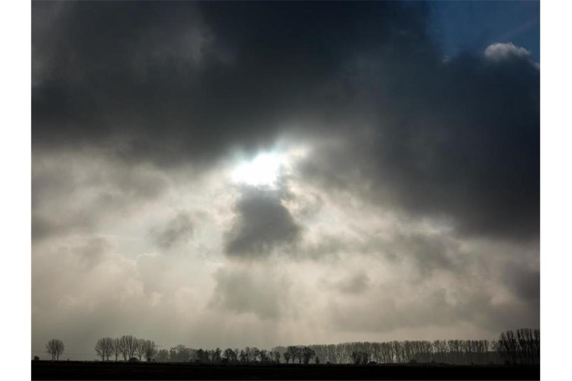 Die Sonne kommt nur kurzzeitig hinter einer dunklen Wolkendecke hervor. Foto: Jens Kalaene/dpa-Zentralbild/ZB/Symbolbild