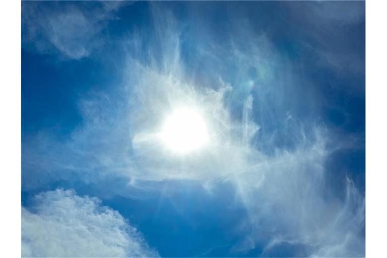 Die Sonne scheint am blauen Himmel durch Wolken hindurch. Foto: Markus Scholz/dpa/Archivbild