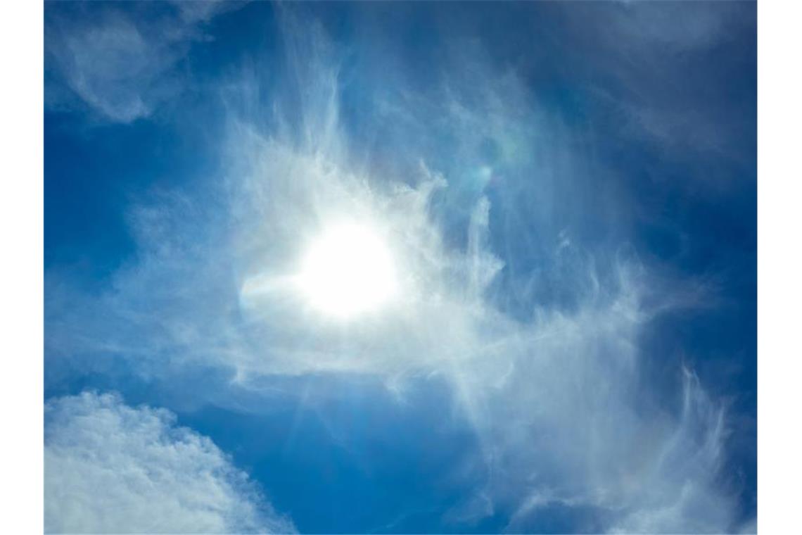 Die Sonne scheint am blauen Himmel durch Wolken hindurch. Foto: Markus Scholz/dpa/Archivbild