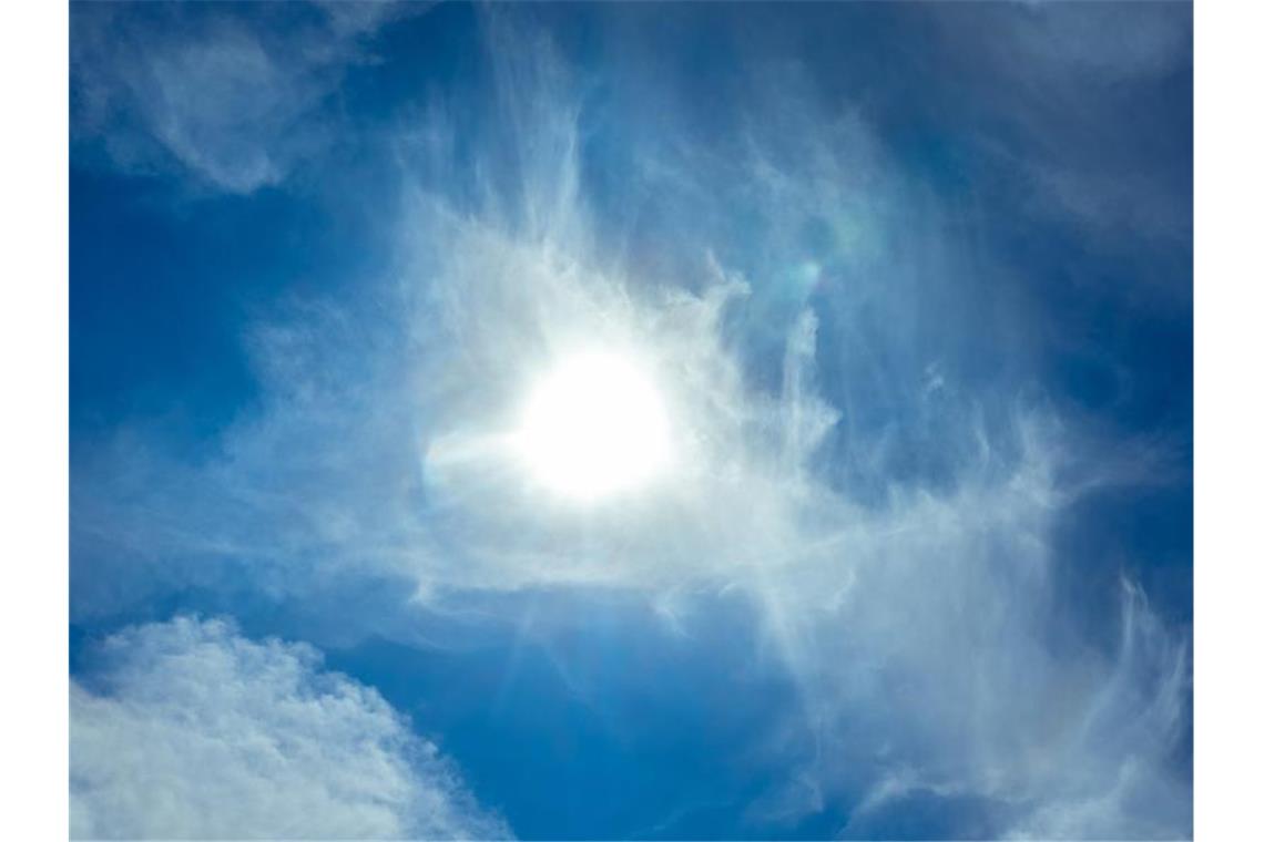 Die Sonne scheint am blauen Himmel durch Wolken hindurch. Foto: Markus Scholz/dpa/Symbolbild