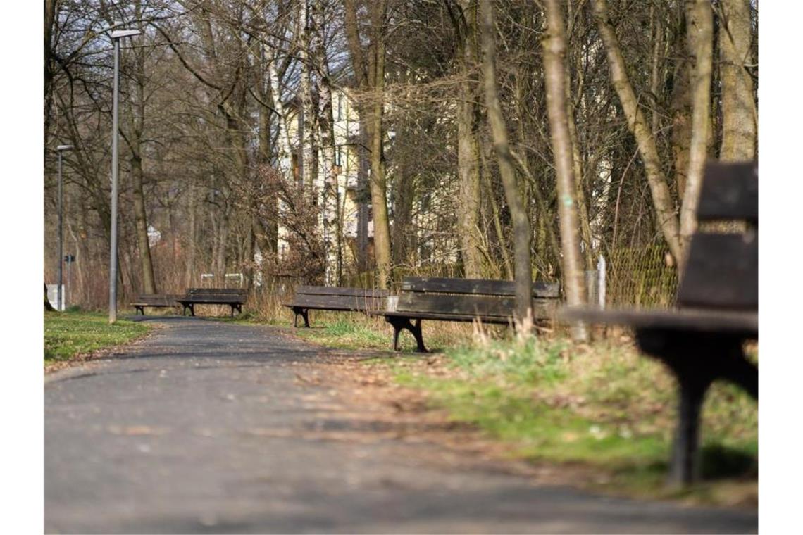 Die Sonne scheint auf leere Sitzbänke entlang eines Fußgängerweges. Foto: Nicolas Armer/dpa/Symbolbild