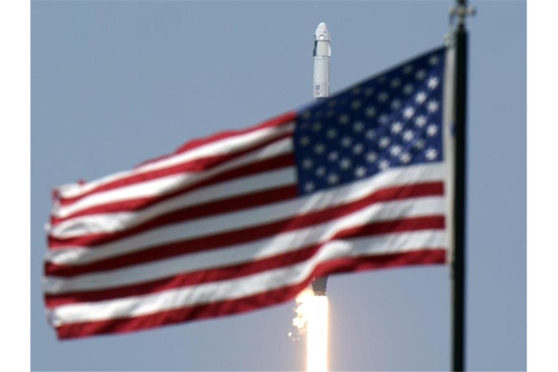 Die SpaceX „Falcon 9“-Rakete hinter einer US-amerikanischen Nationalflagge. Foto: David J. Phillip/AP/dpa