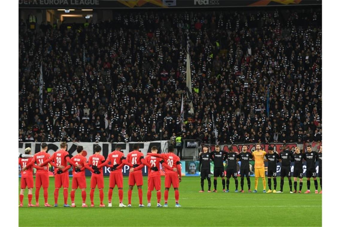 Die Spieler von Eintracht Frankfurt (r) und RB Salzburg stehen bei einer Schweigeminute für die Opfer des Anschlags in Hanau zusammen. Foto: Arne Dedert/dpa
