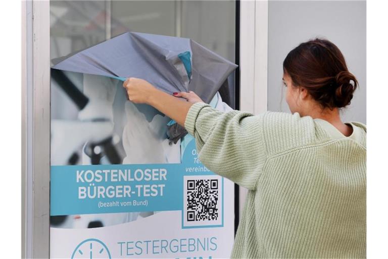 Die Werbeaufkleber eines Corona-Testlabors werden von einer Mitarbeiterin entfernt. Foto: Roland Weihrauch/dpa