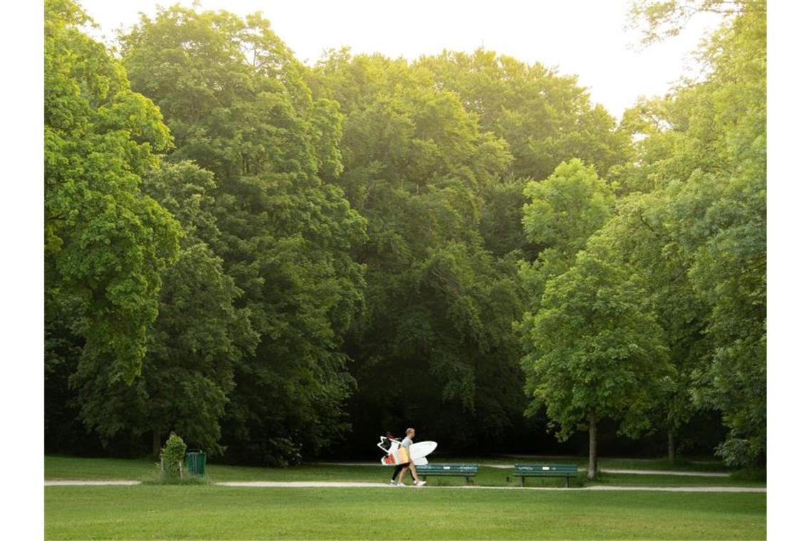 Diese beiden jungen Männer sind mit ihren Surfboards auf dem Weg zum Eisbach im Englischen Garten von München. Foto: Peter Kneffel/dpa