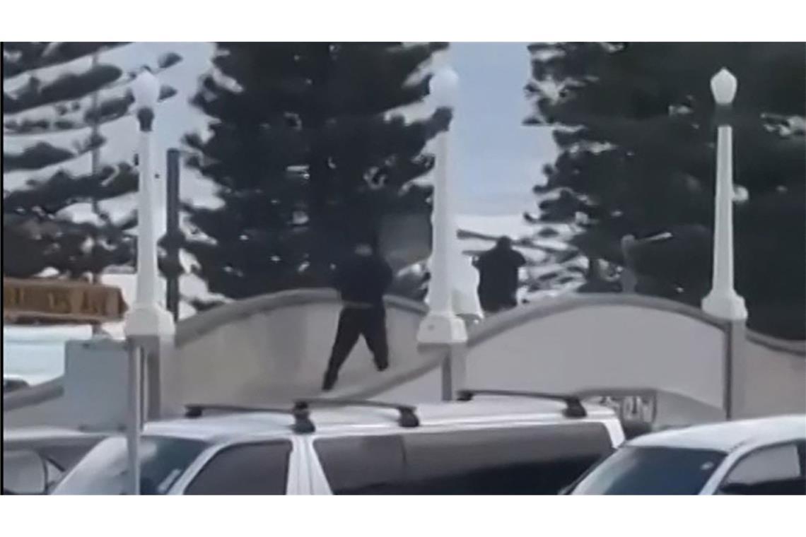 Dieser aus einem von Timothy Brant-Coles zur Verfügung gestellten UGC-Video stammende Bildschirmmitschnitt zeigt zwei schwarz gekleidete bewaffnete Täter, die am 14. Dezember 2025 auf einer Brücke am Bondi Beach in Sydney mehrere Schüsse abfeuern.