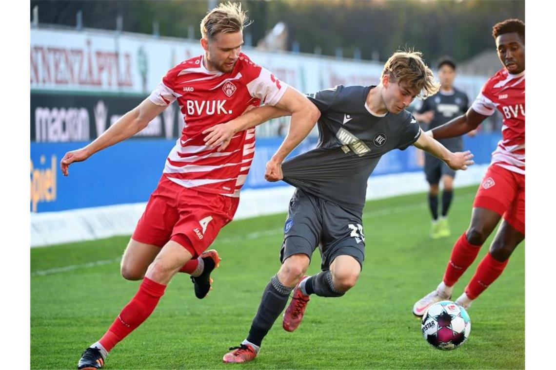 Dominik Kother (M) vom Karlsruher SC und Lars Dietz (l) von den Würzburger Kickers kämpfen um den Ball. Foto: Uli Deck/dpa