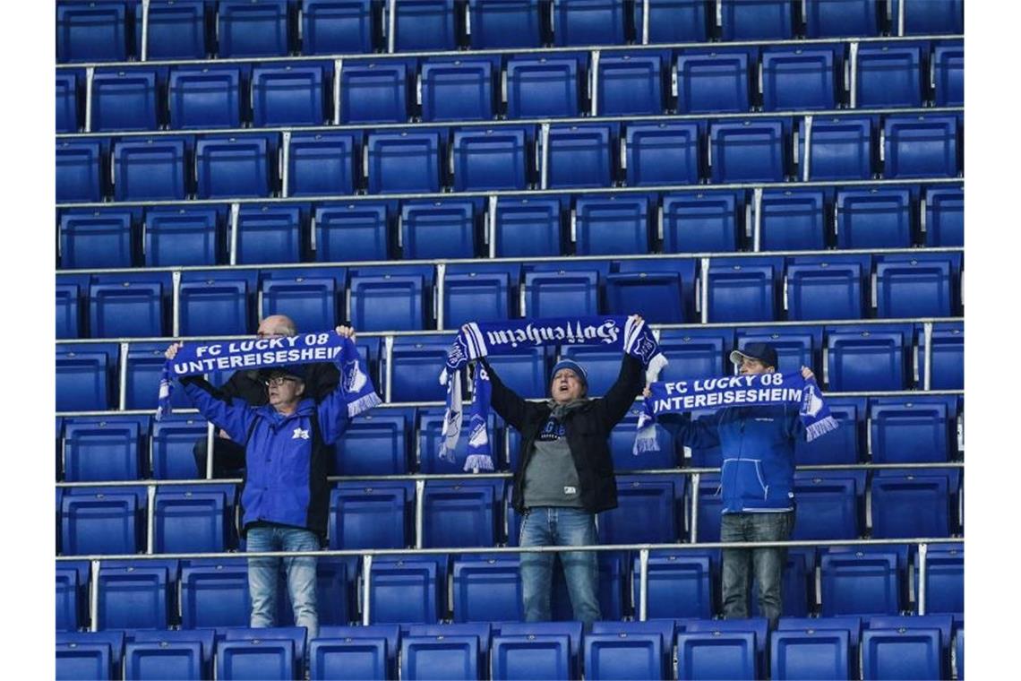 Hoffenheim füllt nur ein Drittel der erlaubten Plätze Drei Hoffenheimer Fans halten vor sonst leeren Zuschauerrängen ihre Fanschals in die Höhe. Foto: Uwe Anspach/dpa
