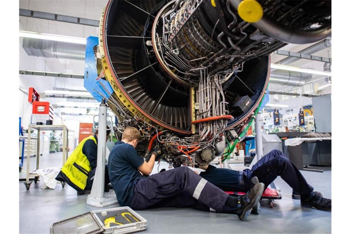 Drei Männer arbeiten in einer Werkstatt von Lufthansa Technik am Triebwerk eines Flugzeuges (Archiv). Foto: Daniel Reinhardt/dpa