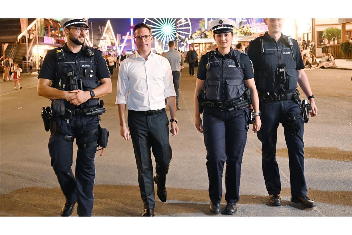 Drei Polizeibeamte in neuen Uniformen der Polizei Baden-Württemberg stehen gemeinsam mit dem baden-württembergischen Innenminister Manuel Hagel (CDU, 2.v.l.) auf dem Cannstatter Wasen. Statt hellblauer Hemden tragen die Beamtinnen und Beamten jetzt häufiger dunkelblaue Poloshirts. Die Kleidung soll mehr Tragekomfort bieten - und besseren Schutz vor Wärme, Kälte und Messerangriffen. (zu dpa: «So kommen die neuen Polizeiuniformen an»)