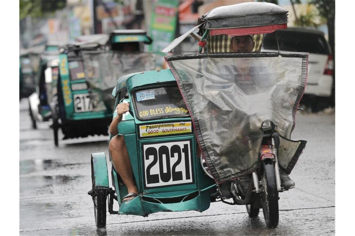 Dreirädrige Mopeds fahren mit Regenschutz durch die Stadt Subic. Foto: Tatan Syuflana/AP/dpa