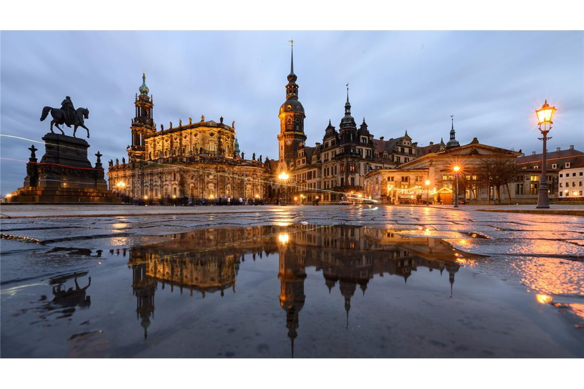 Bilder des Tages Dresden am Abend - Das Reiterstandbild König Johann (l-r), die Hofkirche, der Hausmannsturm, das Residenzschloss und die Schinkelwache spiegeln sich am Abend in einer Pfütze auf dem Theaterplatz.