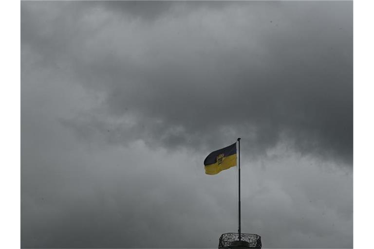 Dunkle Regenwolken über dam Neuen Schloss, auf dem die Flagge von Baden-Württemberg weht. Foto: Bernd Weißbrod/dpa/Archivbild