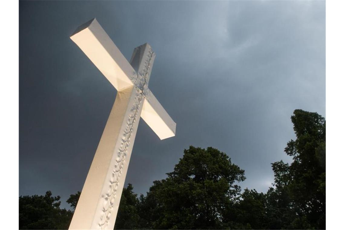Dunkle Wolken über einem Kreuz. Foto: picture alliance / Lino Mirgeler/dpa
