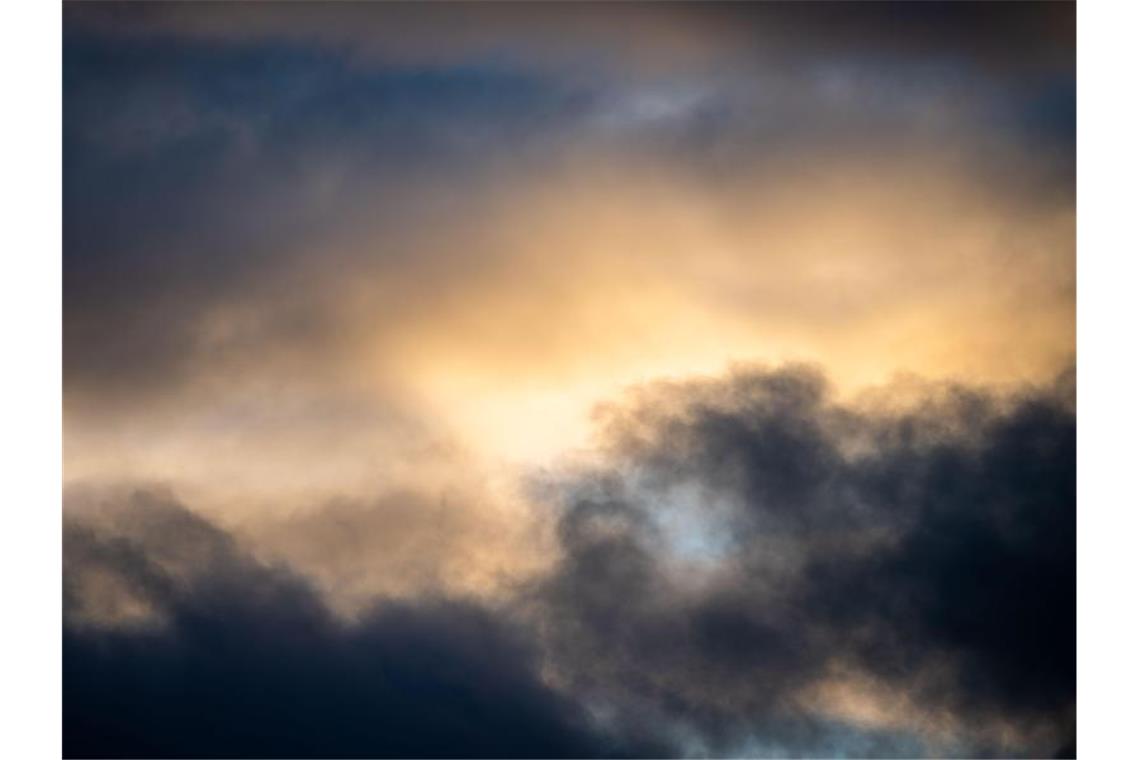 Dunkle Wolken vermischen sich beim Sonnenuntergang. Foto: Lino Mirgeler/dpa/Archivbild