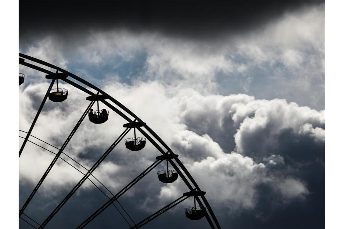 Dunkle Wolken ziehen beim 174. Cannstatter Volksfest hinter einem Riesenrad vorbei. Foto: Christoph Schmidt