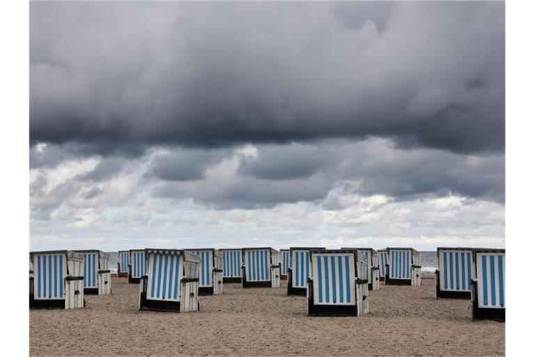 Dunkle Wolken ziehen über den Ostseestrand von Warnemünde. Sommerliches Wetter ist vorerst nicht in Sicht. Foto: Bernd Wüstneck/dpa-Zentralbild/dpa