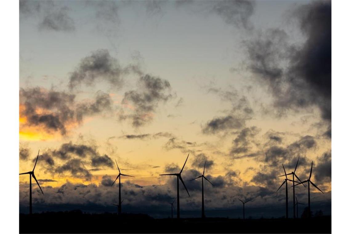 Dunkle Wolken ziehen vor einem orange gefärbtem Himmel über Windräder hinweg. Foto: Moritz Frankenberg/dpa