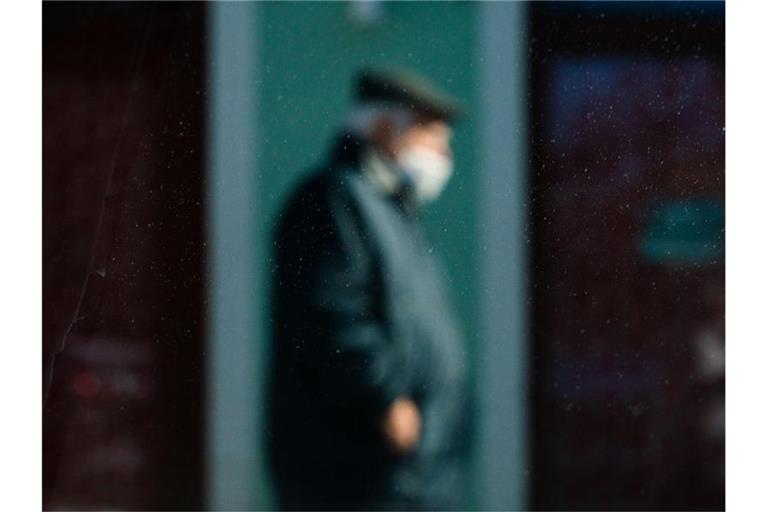Durch eine Scheibe fotografiert, ist ein Mann mit Mund-Nasen-Schutz schemenhaft zu erkennen. Foto: Nicolas Armer/dpa/Archivbild