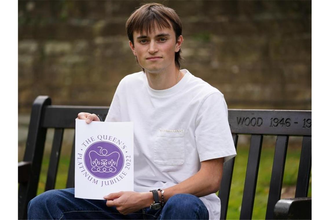 Edward Roberts hält sein Logo zum 70. Thronjubiläum von Queen Elizabeth II. im nächsten Jahr hoch. Bei einem Wettbewerb für junge Designer hat man den Entwurf des 19-jährigen Roberts ausgewählt. Foto: Jacob King/PA Wire/dpa