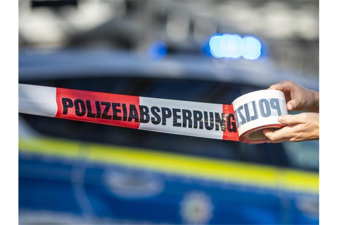 Ein Absperrband wird vor einem Polizeiwagen ausgerollt. Foto: David Inderlied/dpa/Illustration