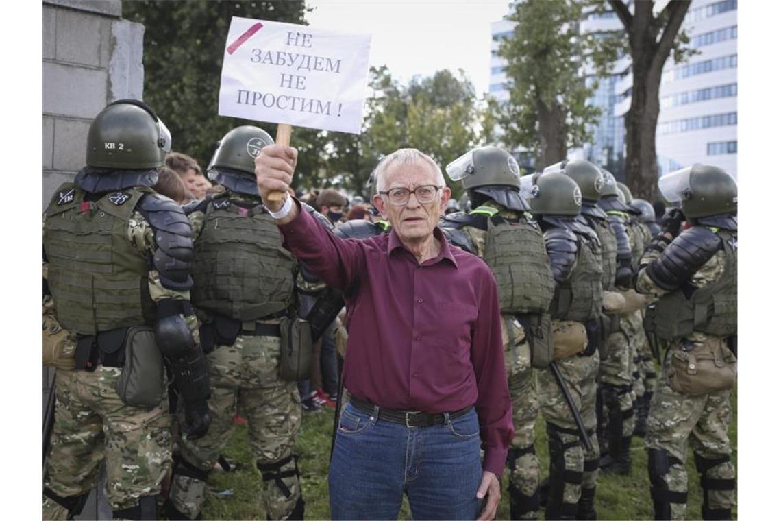 Ein älterer Demonstrant steht bei einem Protest der belarussischen Opposition gegen die Ergebnisse der Präsidentenwahl vor einer Gruppe von Polizisten und hält ein Schild mit der Aufschrift „Wir werden nicht vergessen, wir werden nicht verzeihen“ in der Hand. Foto: -/Tut.by via AP/dpa
