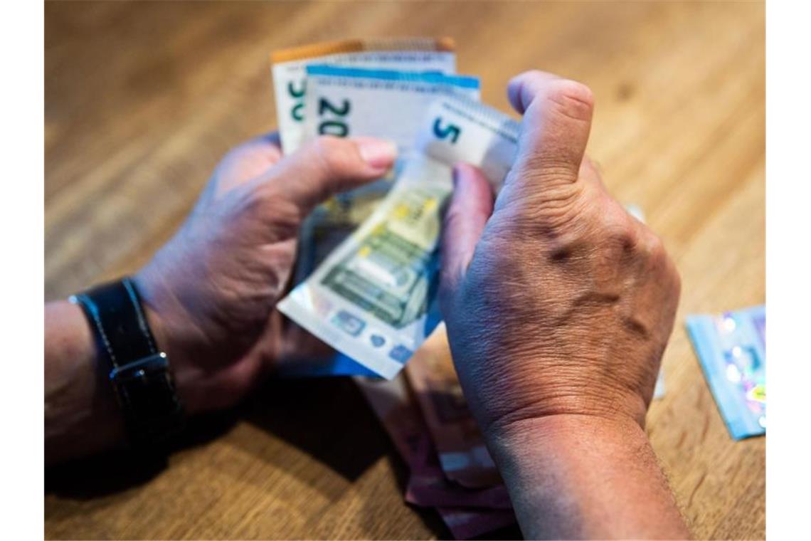 Ein älterer Mann zählt Geld an einem Tisch. Foto: Lino Mirgeler/dpa/Illustration