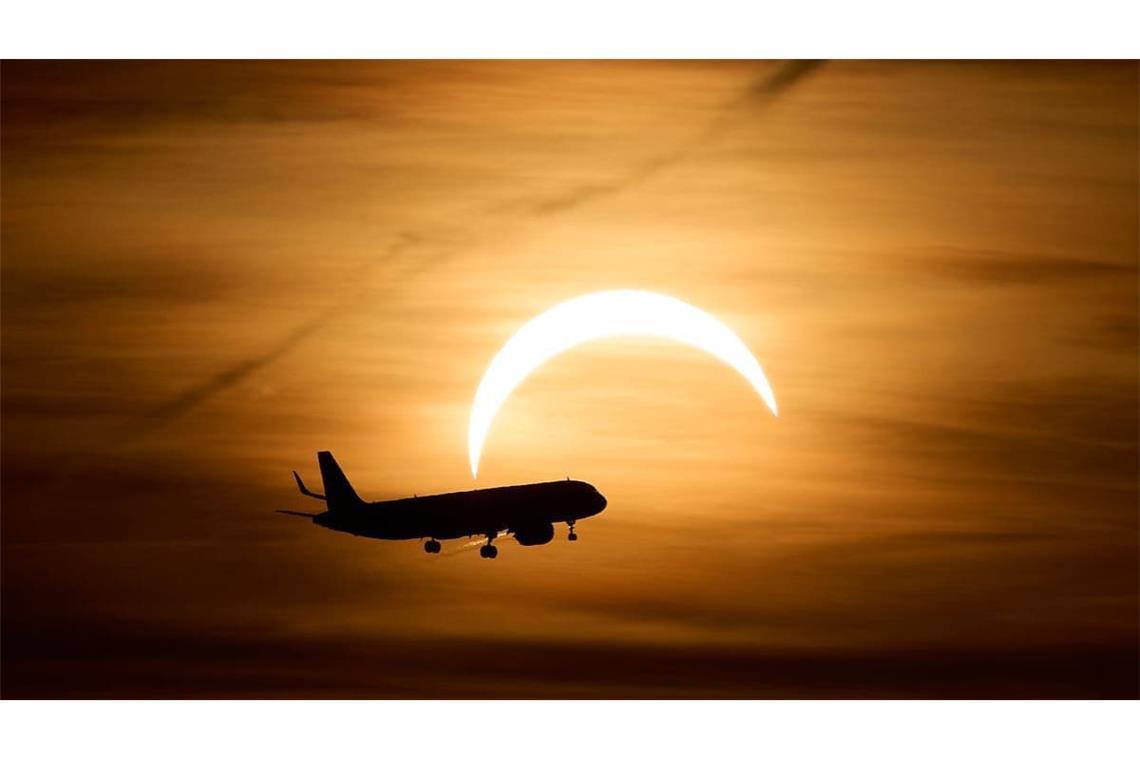 Ein Airbus A321 aus London fliegt während der partiellen Sonnenfinsternis im Landeanflug auf den Flughafen Berlin Brandenburg (BER) vor der teilweise vom Mond verdeckten Sonne. 