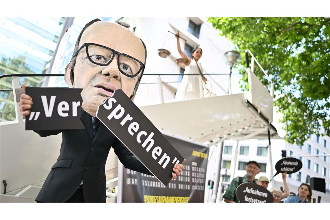 Aufnahme von Afghanen - Klagen gegen Bundesregierung Ein Aktivist mit Merz-Maske zerbricht während einer symbolischen Protestaktion von Kabul Luftbrücke und Campact ein Schild mit der Aufschrift "Versprechen".