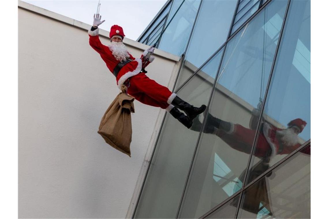 Ein als Weihnachtsmann verkleideter Feuerwehrmann seilt sich an der Glasfassade der Kinderklinik ab. Foto: Stefan Puchner/dpa