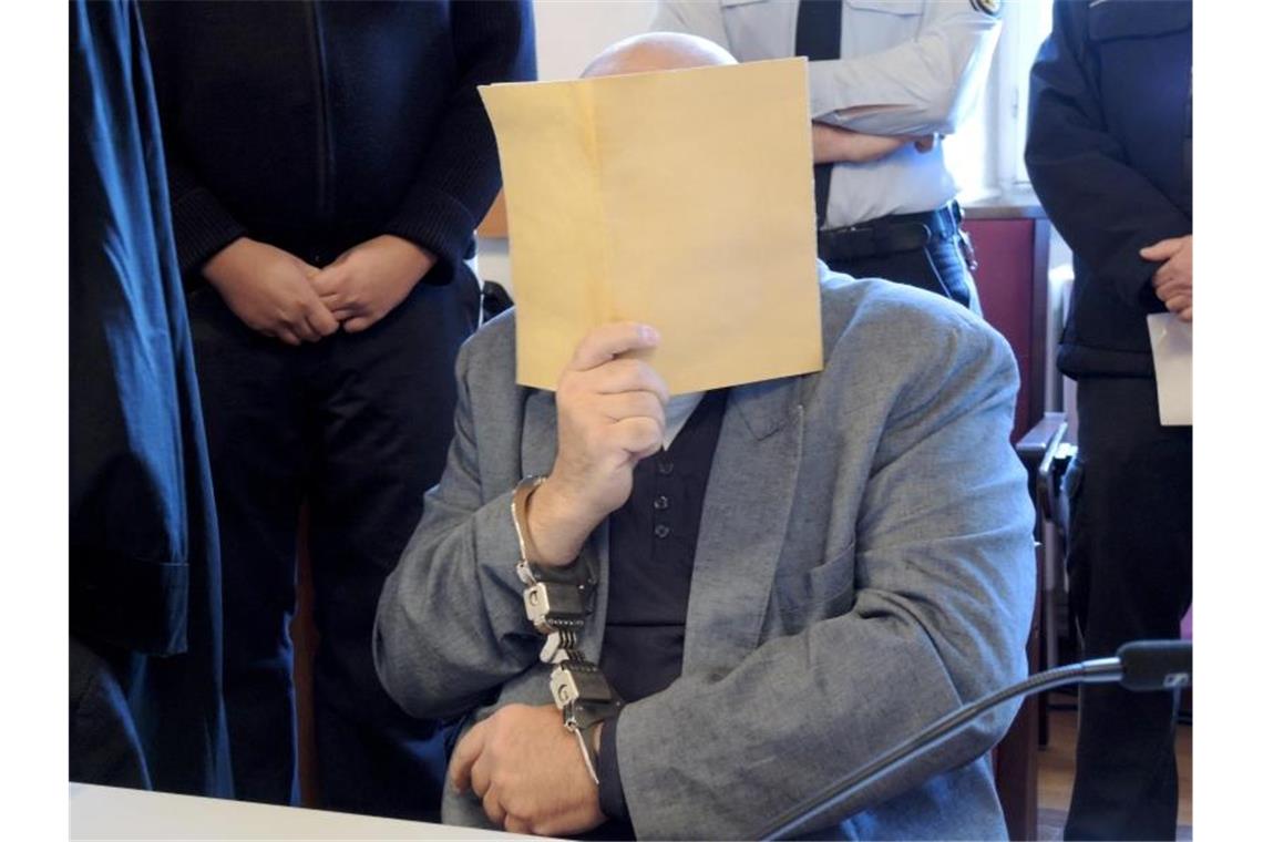 Ein Angeklagter sitzt mit einem Aktendeckel zum Schutz vor Fotos im Gerichtssaal. Foto: Thomas Burmeister/dpa
