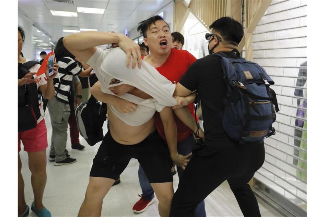 Ein Anhänger der Führung in Peking in einem roten T-Shirt und regierungskritische Demonstranten leisten sich handgreifliche Auseinandersetzungen. Foto: Kin Cheung/AP