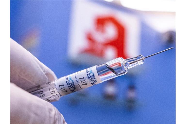 Ein Apotheker hält eine Spritze mit Impfstoff vor dem Logo der Apotheke. Foto: David Inderlied/dpa/Symbolbild
