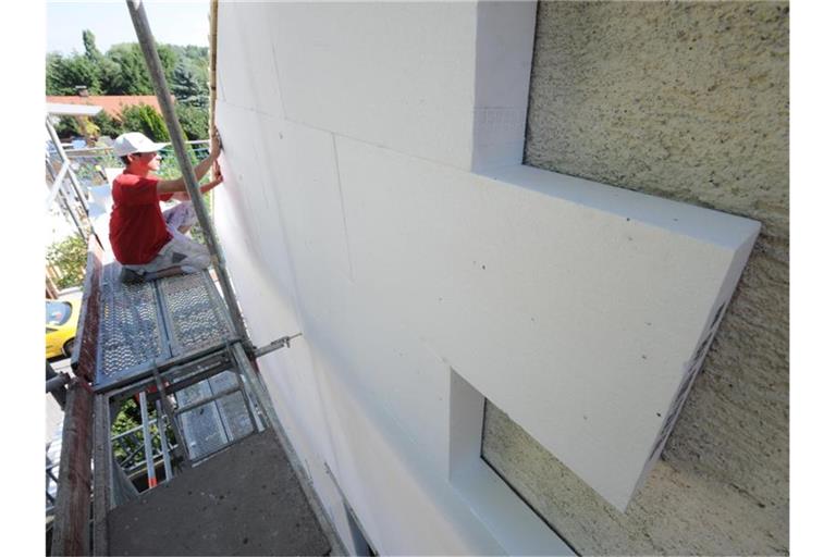 Ein Arbeiter befestigt Styroporplatten zur Wärmedämmung an einer Hausfassade. Foto: Armin Weigel