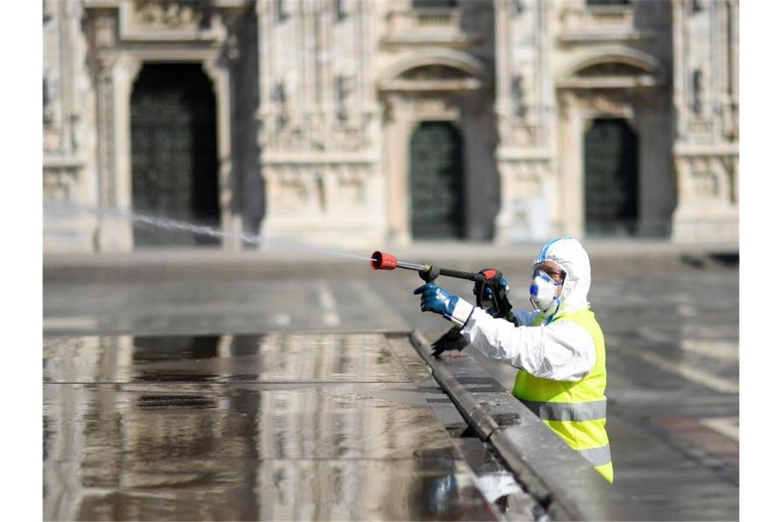Kampf gegen Corona: Italien verlängert Ausgangsverbote Ein Arbeiter in Schutzanzug reinigt den Piazza del Duomo in Mailand. Foto: Daniele Mascolo/XinHua/dpa