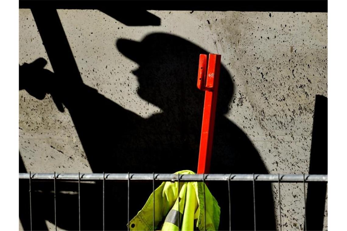 Ein Arbeiter ist auf einer Baustelle beschäftigt und wirft dabei einen dunklen Schatten. Die Wirtschaftsleistung in Deutschland ist im zweiten Quartal in Folge der Corona-Krise erheblich eingebrochen. Foto: Ralf Hirschberger/dpa-Zentralbild/dpa