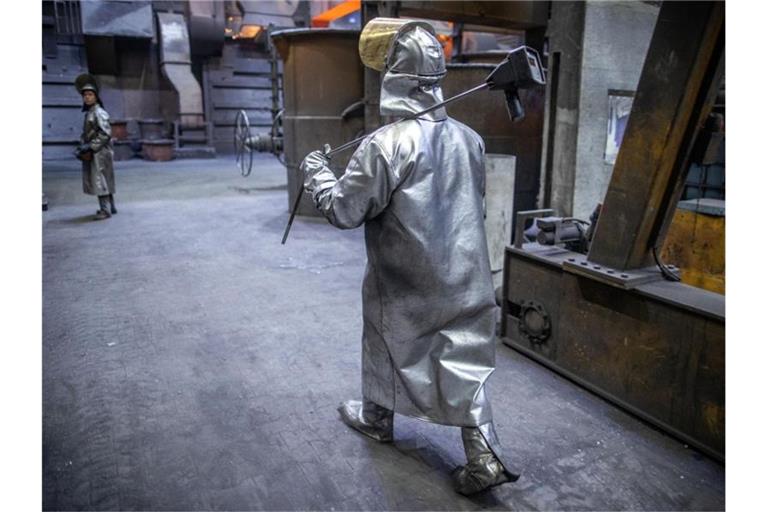 Ein Arbeiter mit Schutzbekleidung und Helm geht zu den Schmelzöfen in einer Eisengießerei in Torgelow (Mecklenburg-Vorpommern). Foto: Jens Büttner/dpa-Zentralbild/dpa