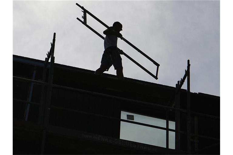 Ein Arbeiter trägt auf einer Baustelle ein Teil eines Baugerüsts. Foto: Britta Pedersen/dpa-Zentralbild/dpa/Symbolbild